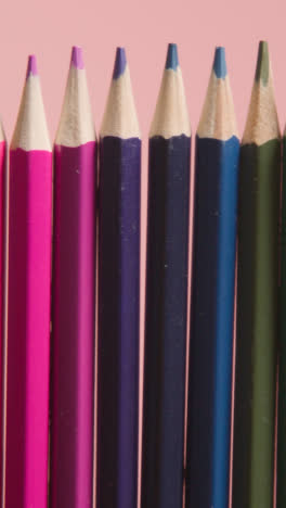 Vertical-Video-Studio-Shot-Of-Multi-Coloured-Pencils-In-A-Line-On-Pink-Background-1